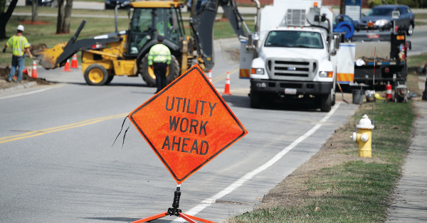 An image with an orange construction sign reading "Utility work ahead" with workers and trucks in the background.